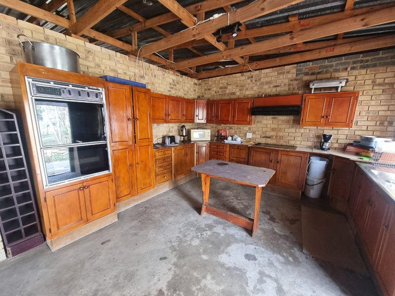 A rustic kitchen featuring exposed brick walls, timber roof trusses, built-in wooden cabinetry, and a double oven, offering significant potential for modernization.