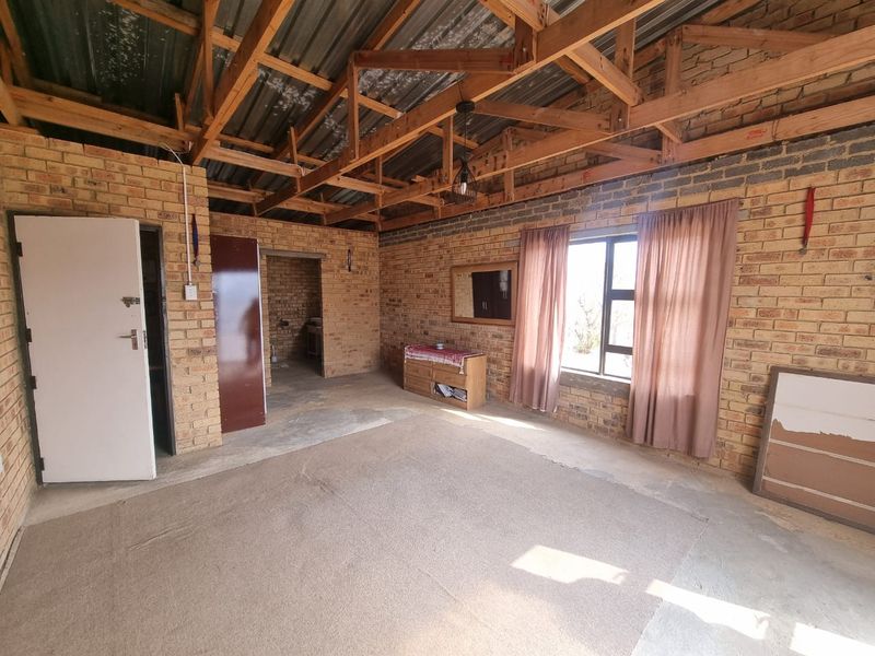 An unfinished living area featuring exposed timber roof trusses, face brick walls, and concrete flooring, offering a blank canvas for renovation.