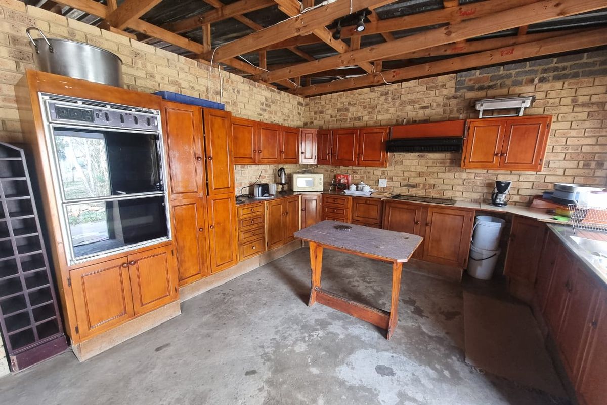 A rustic kitchen featuring exposed brick walls, timber roof trusses, built-in wooden cabinetry, and a double oven, offering significant potential for modernization.
