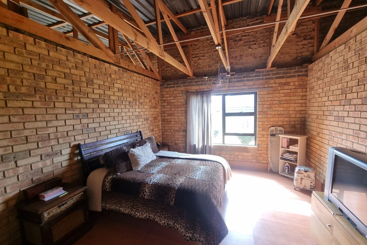 A rustic bedroom featuring exposed timber roof trusses and facebrick walls, offering a unique industrial aesthetic with potential for modern interior design updates.