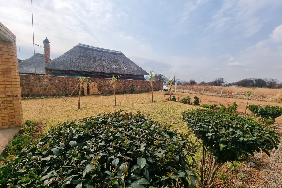 A view of the rear garden featuring a stone boundary wall and a traditional thatched roof structure.