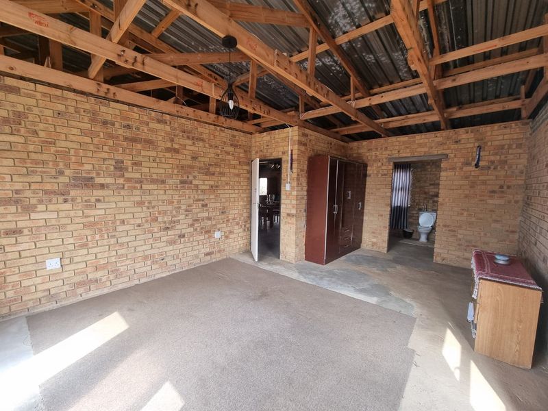 Open-plan living area featuring exposed timber roof trusses, facebrick walls, and concrete flooring, with direct access to an adjoining bathroom.