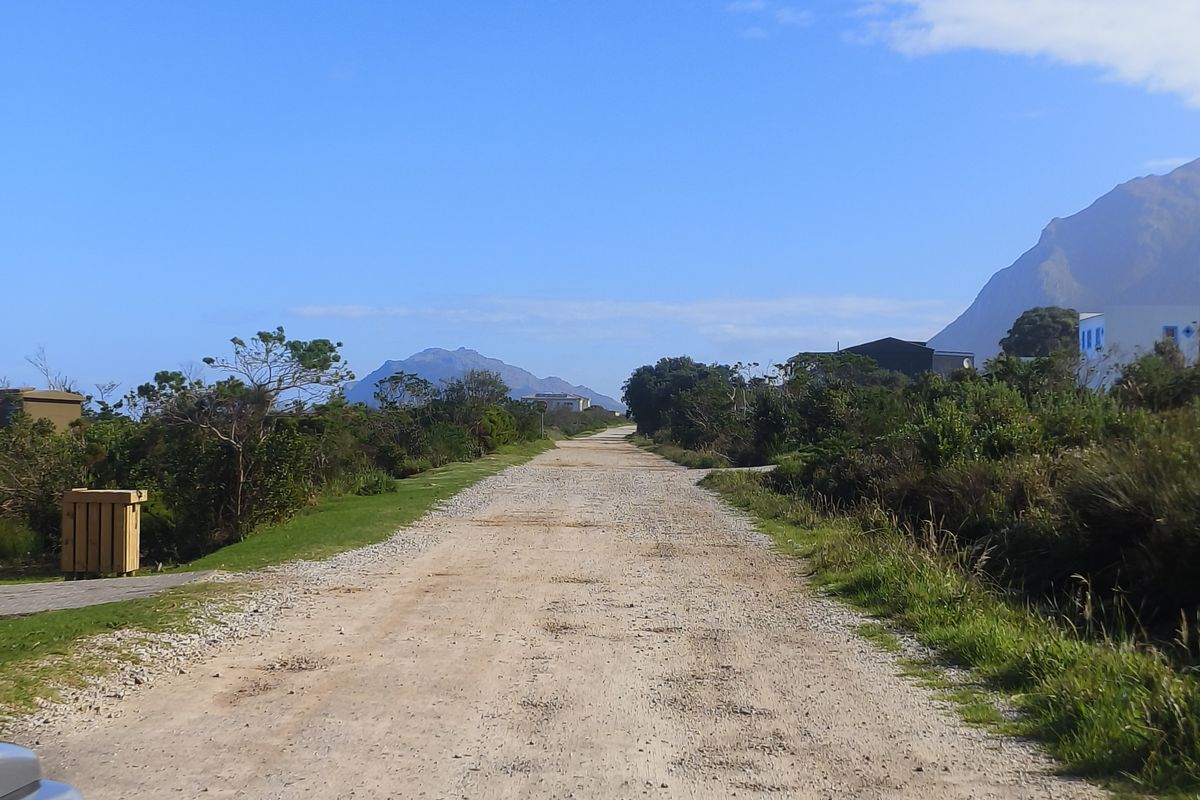 A view of an unpaved residential access road surrounded by natural vegetation and mountain scenery.