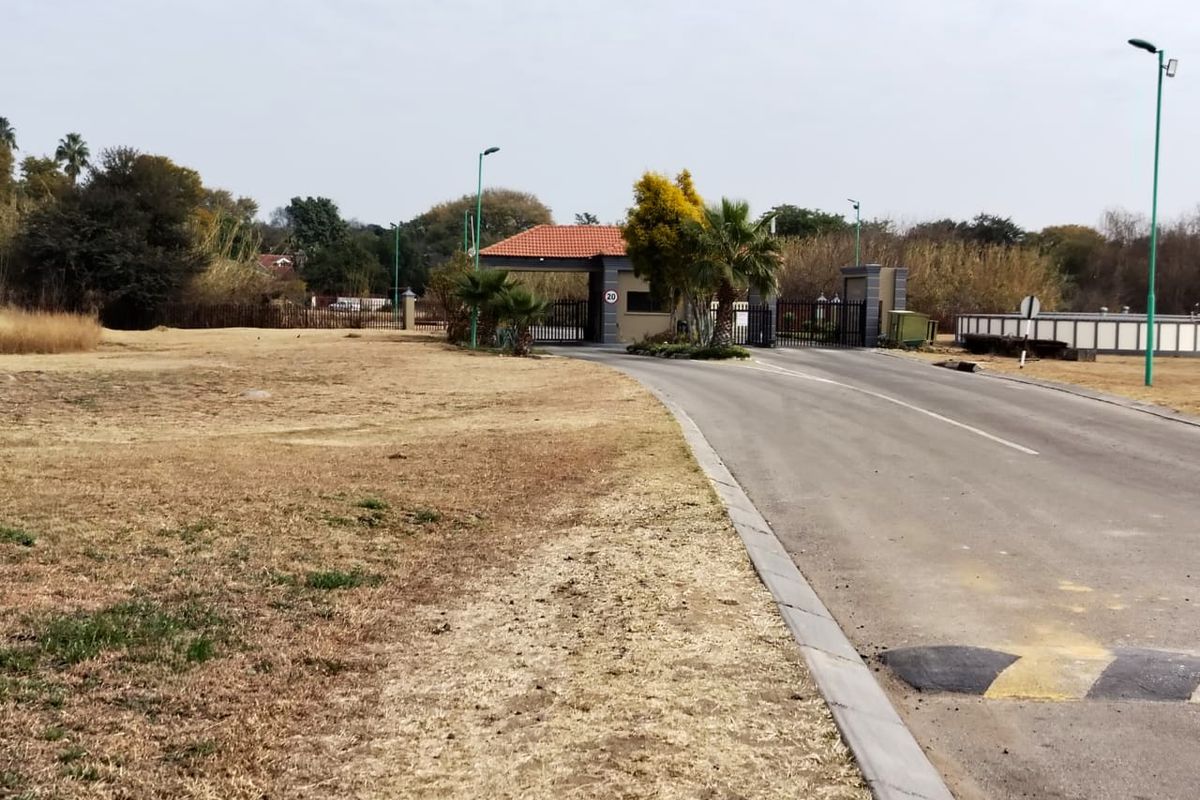 View of the residential estate entrance featuring a security gatehouse, paved access road, and established landscaping.