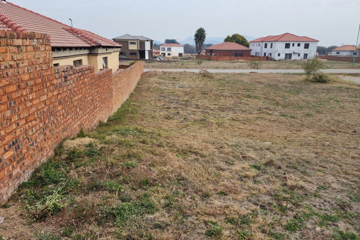 A vacant residential plot featuring a brick boundary wall, situated in a developed neighborhood with surrounding houses.