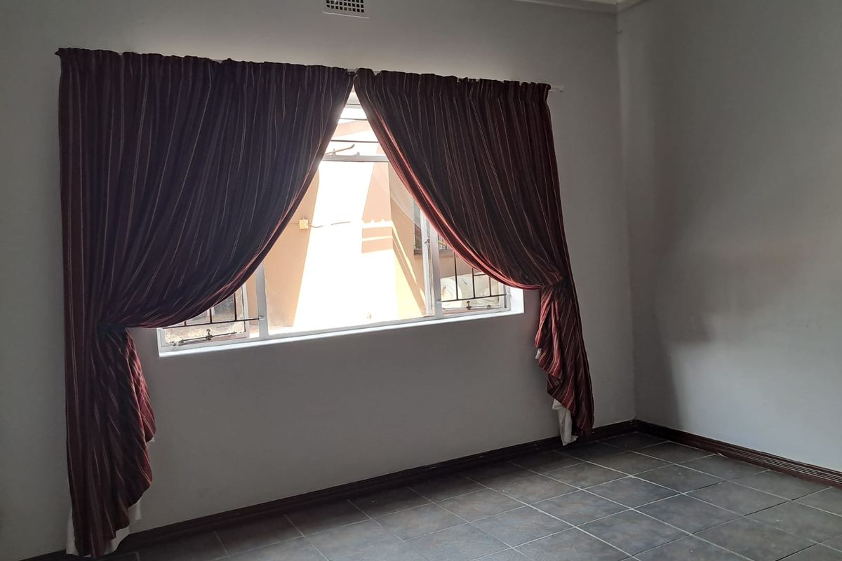 An empty bedroom featuring tiled flooring, a window with security bars, and a ceiling air vent.