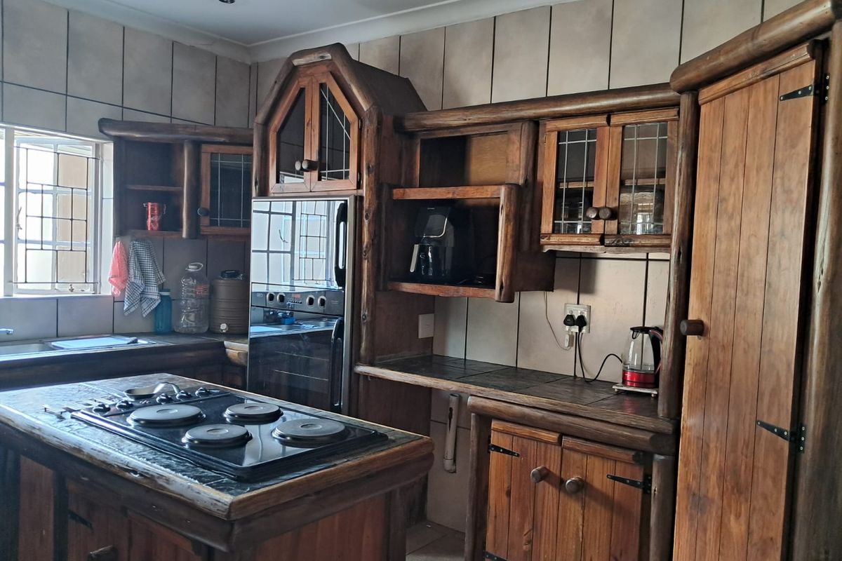 A rustic-style kitchen featuring custom wooden cabinetry, a central island with an integrated electric cooktop, and tiled splashbacks.