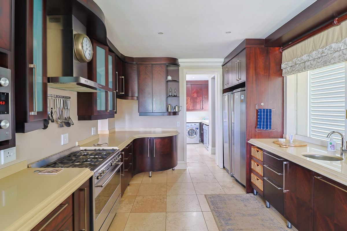A well-appointed kitchen featuring dark wood cabinetry, stone countertops, a gas cooktop, and integrated appliances, with an adjacent scullery area visible.