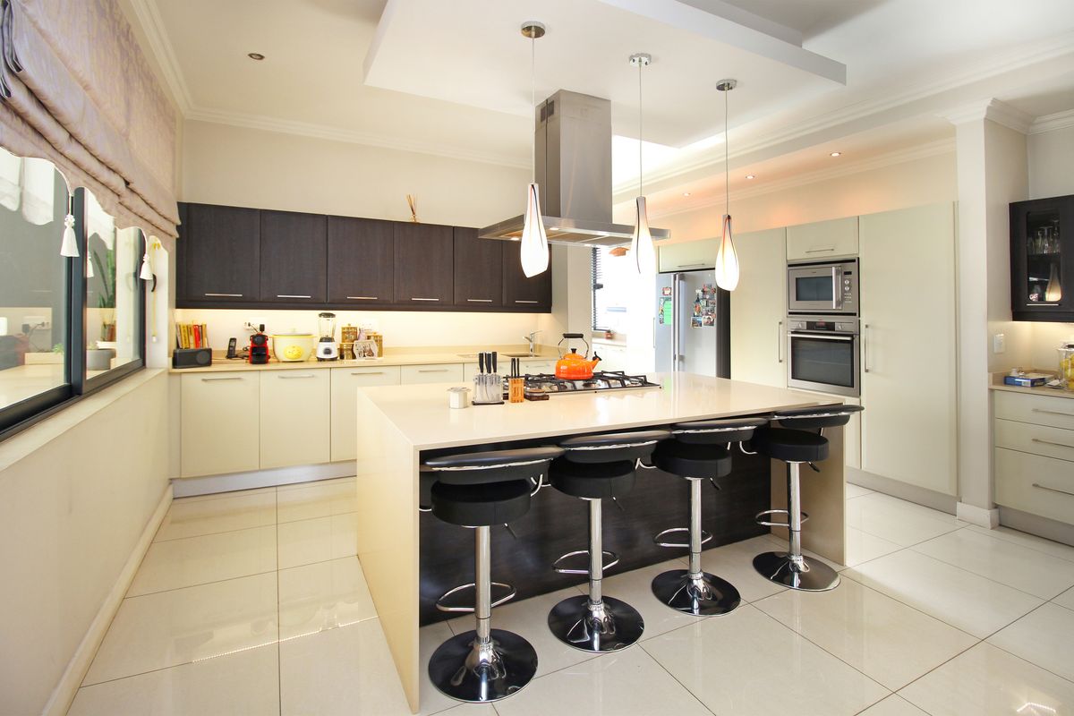 Modern kitchen featuring a central island with breakfast bar, built-in oven and microwave, stainless steel extractor fan, and sleek cabinetry with stone countertops.