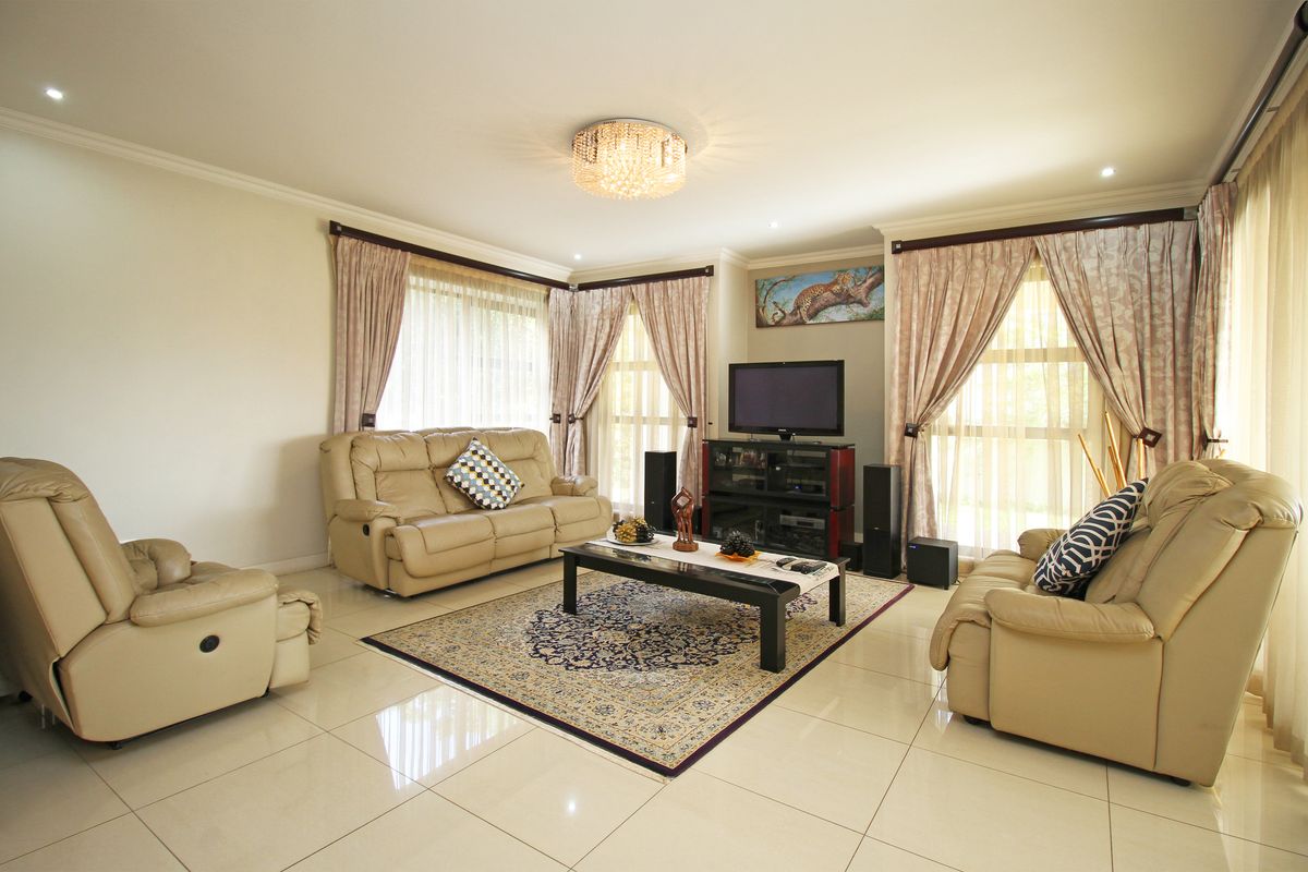 A spacious and well-lit living room featuring polished floor tiles, recessed downlighting, and large windows with elegant curtain treatments.