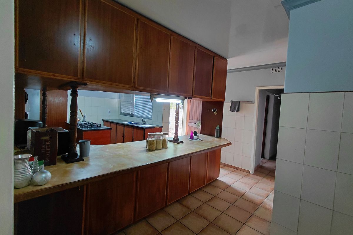A functional kitchen featuring extensive wooden cabinetry, laminate countertops, and tiled flooring, with a pass-through window connecting to the adjacent workspace.