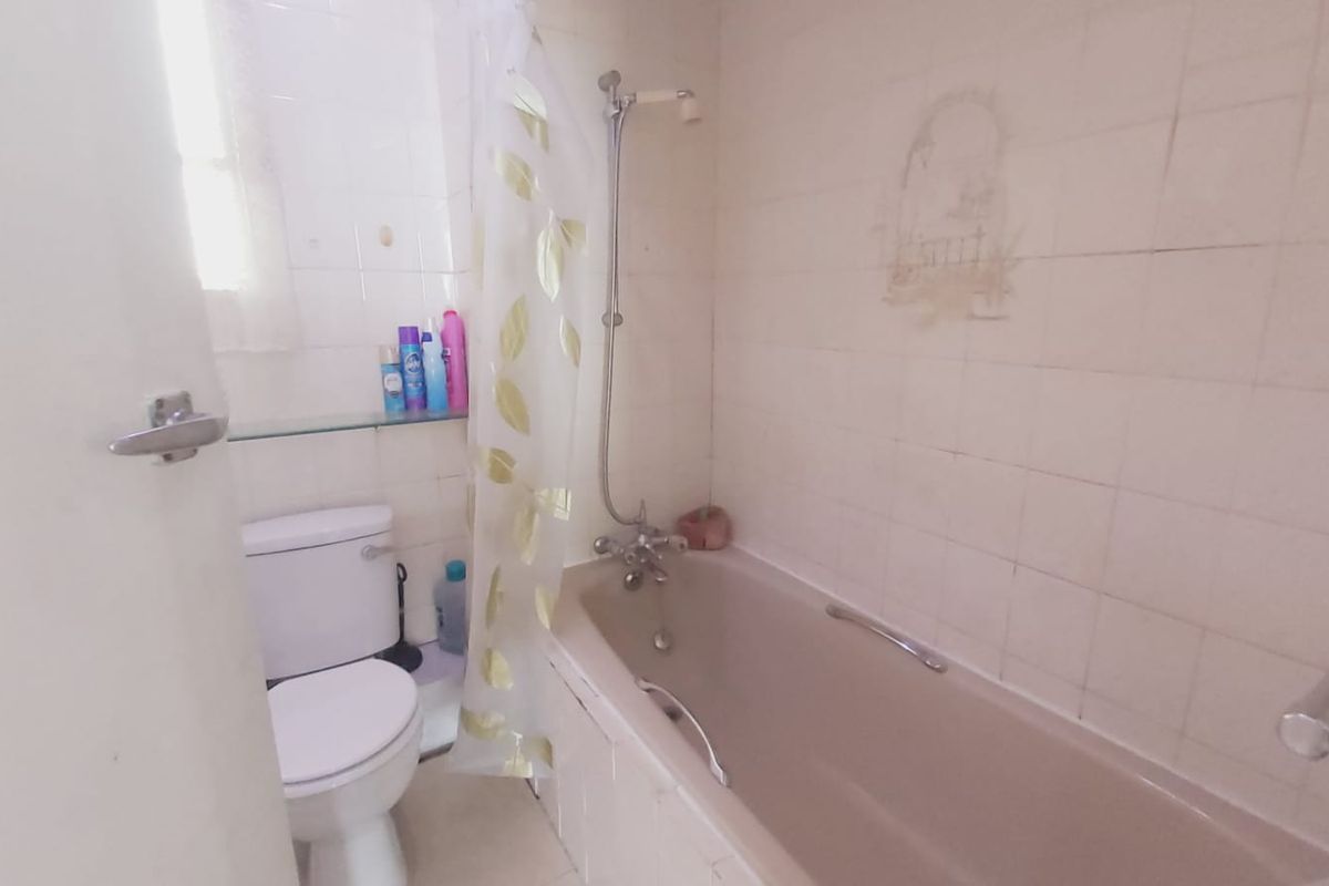 A functional bathroom featuring a bathtub with shower mixer, toilet, and grab rail, finished with tiled walls.