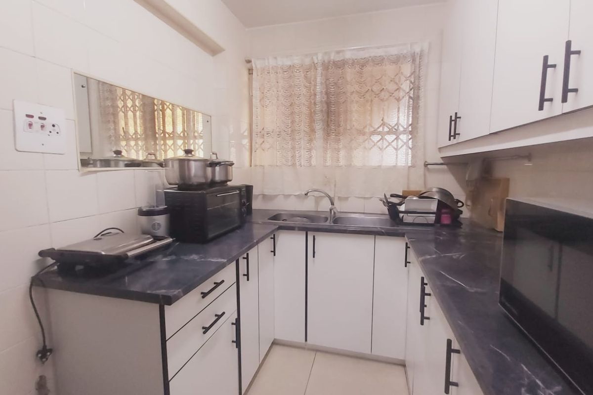 A functional kitchen featuring white cabinetry, dark laminate countertops, a double basin sink, and tiled splashbacks, providing a practical workspace.