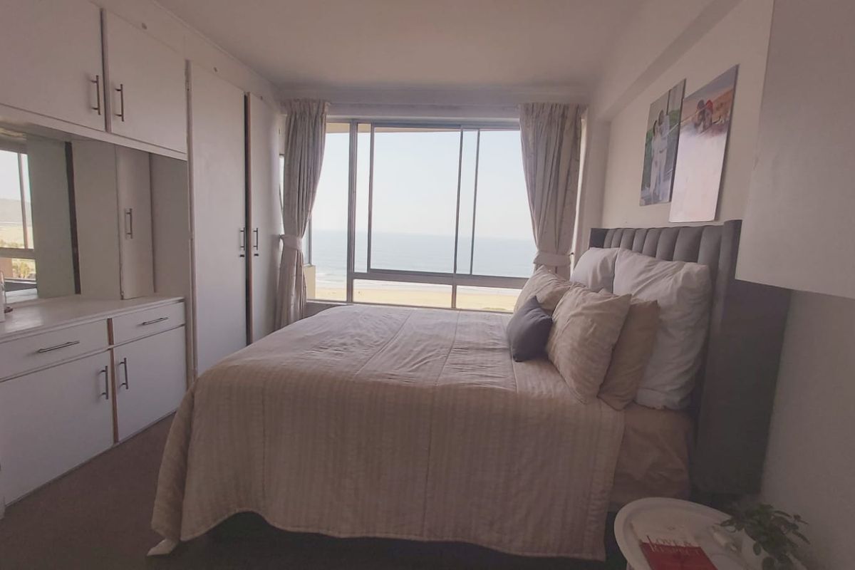 A bedroom featuring built-in cupboards, a vanity unit, and large sliding windows offering direct ocean views.