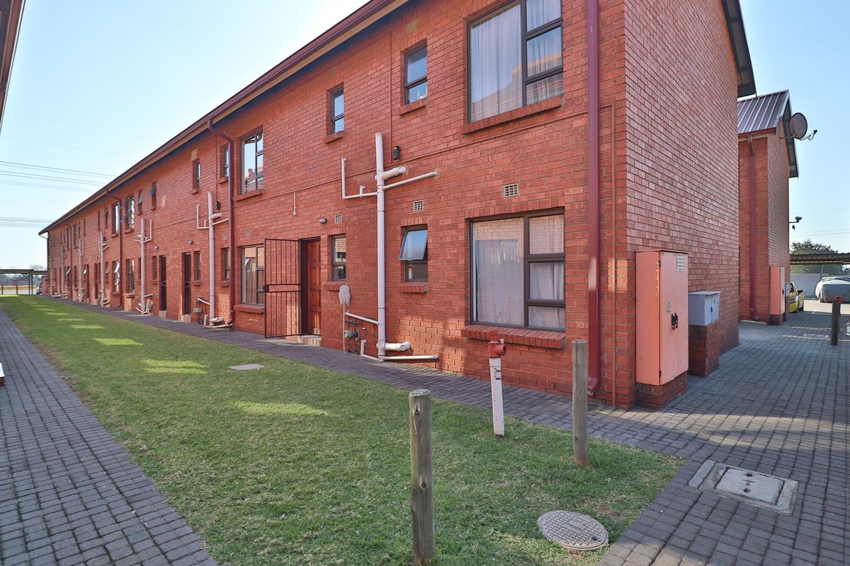 Exterior view of a multi-story apartment block featuring face brick construction, paved walkways, and communal garden space.