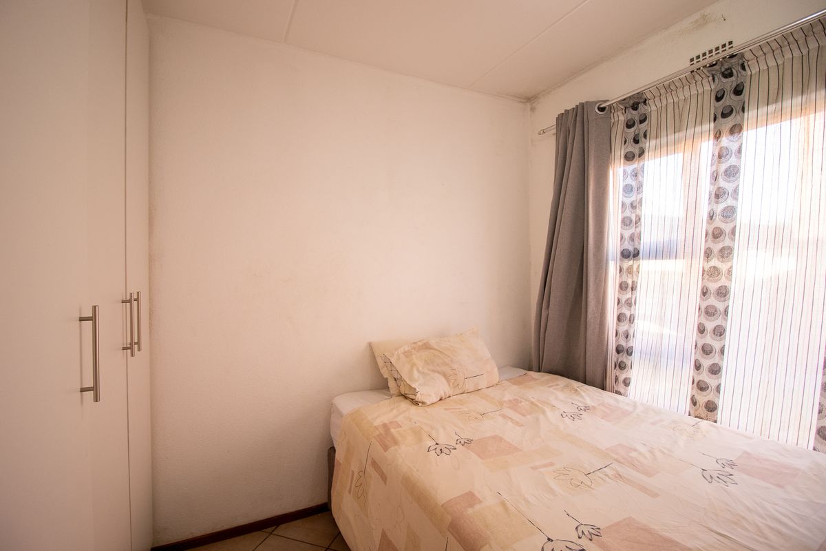 A compact bedroom featuring built-in wardrobes, tiled flooring, and natural light from a window with curtain fixtures.