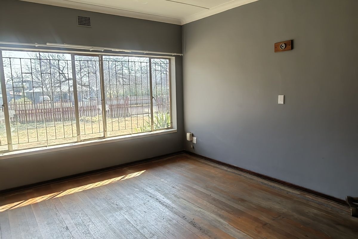 A vacant bedroom featuring original timber flooring, large windows with security bars, and neutral grey wall paint, offering a blank canvas for renovation.