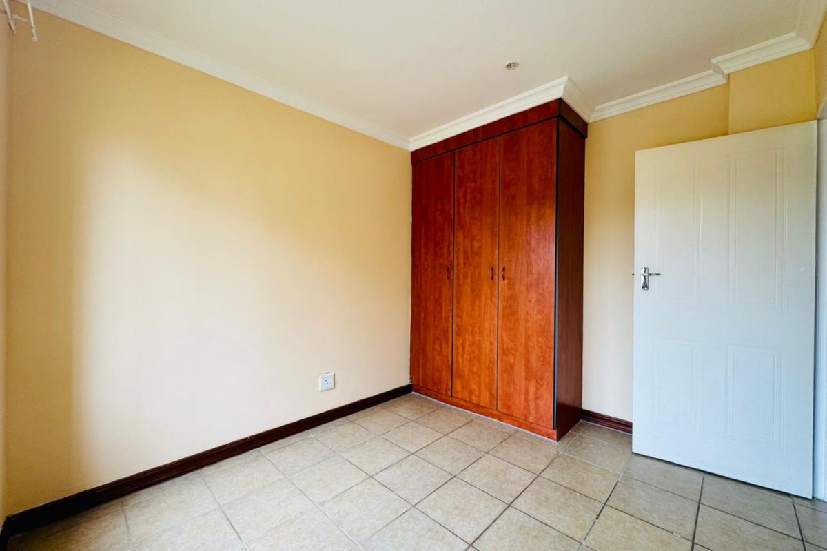 A clean, empty bedroom featuring tiled flooring, built-in wooden cabinetry, and crown molding, offering a neutral canvas for personalization.