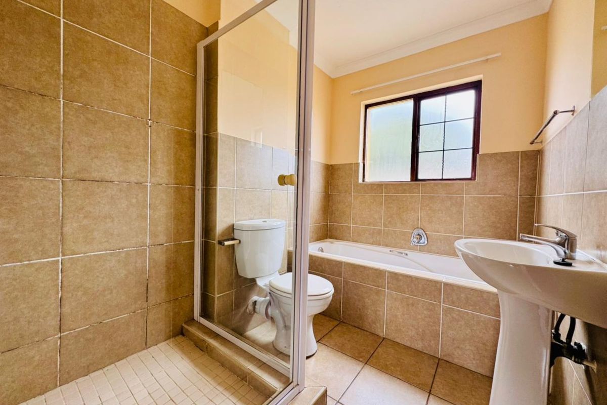 A functional bathroom featuring a tiled shower enclosure, a built-in bathtub, and a pedestal basin with neutral wall tiling.