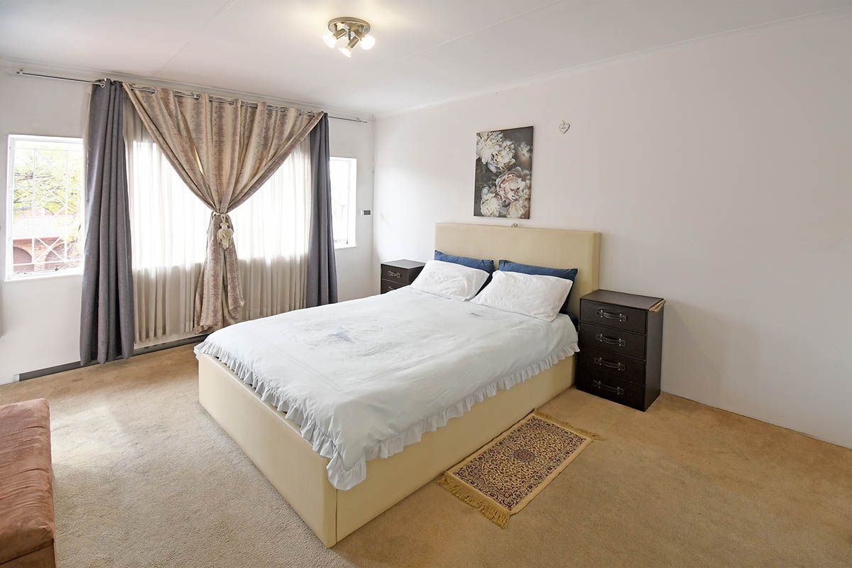 A spacious bedroom featuring neutral walls, carpeted flooring, and large windows with curtain treatments, providing a comfortable and functional living space.