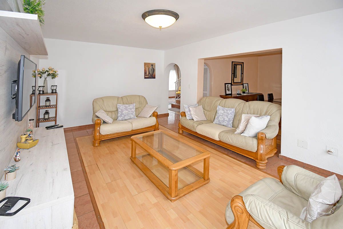 A comfortable living room featuring a mix of tiled and wood-look flooring, with an arched entryway leading to an adjacent dining area.