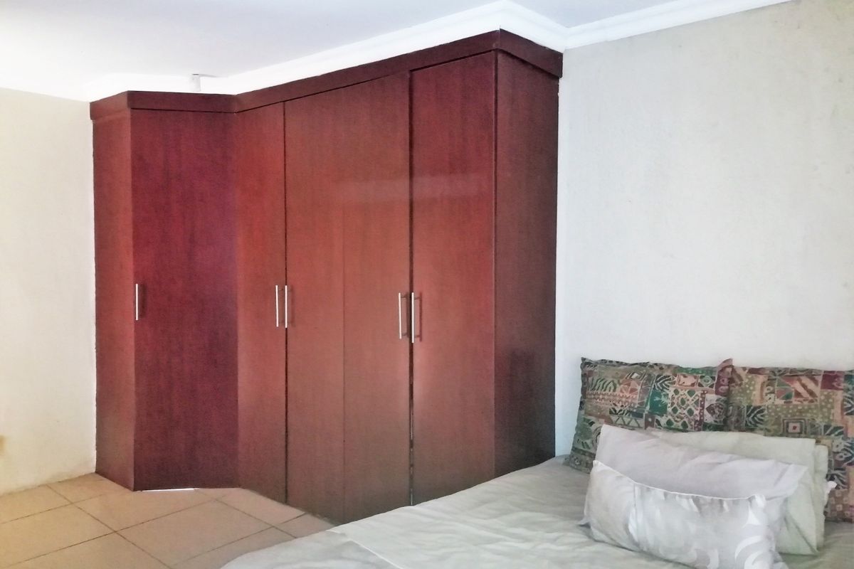 A bedroom featuring a large, dark wood built-in wardrobe, tiled flooring, and coved ceiling details.