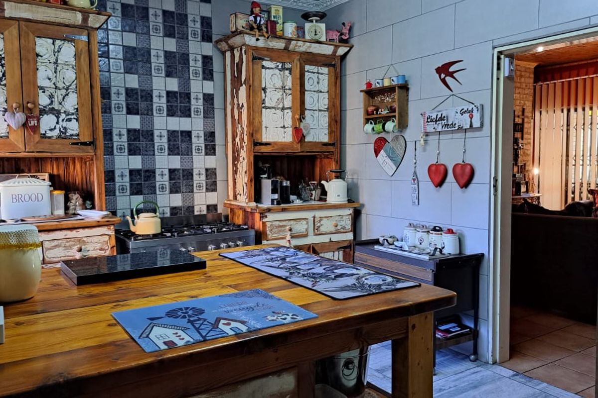 A rustic-style kitchen featuring wooden cabinetry, a gas stove, and a central wooden island, with a doorway leading to an adjacent living area.