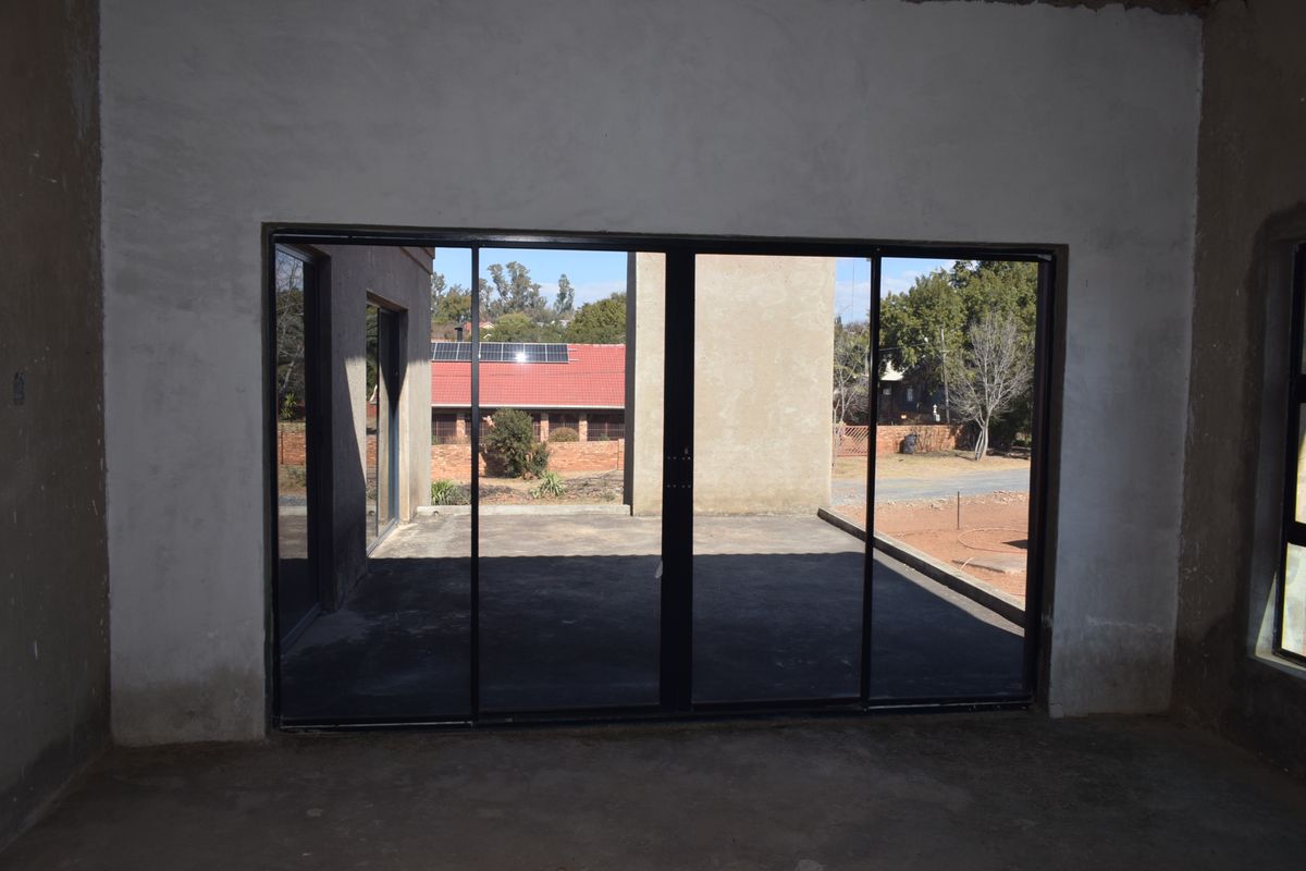 An unfinished interior space featuring large sliding glass doors that open onto an outdoor patio area, providing a blank canvas for renovation.