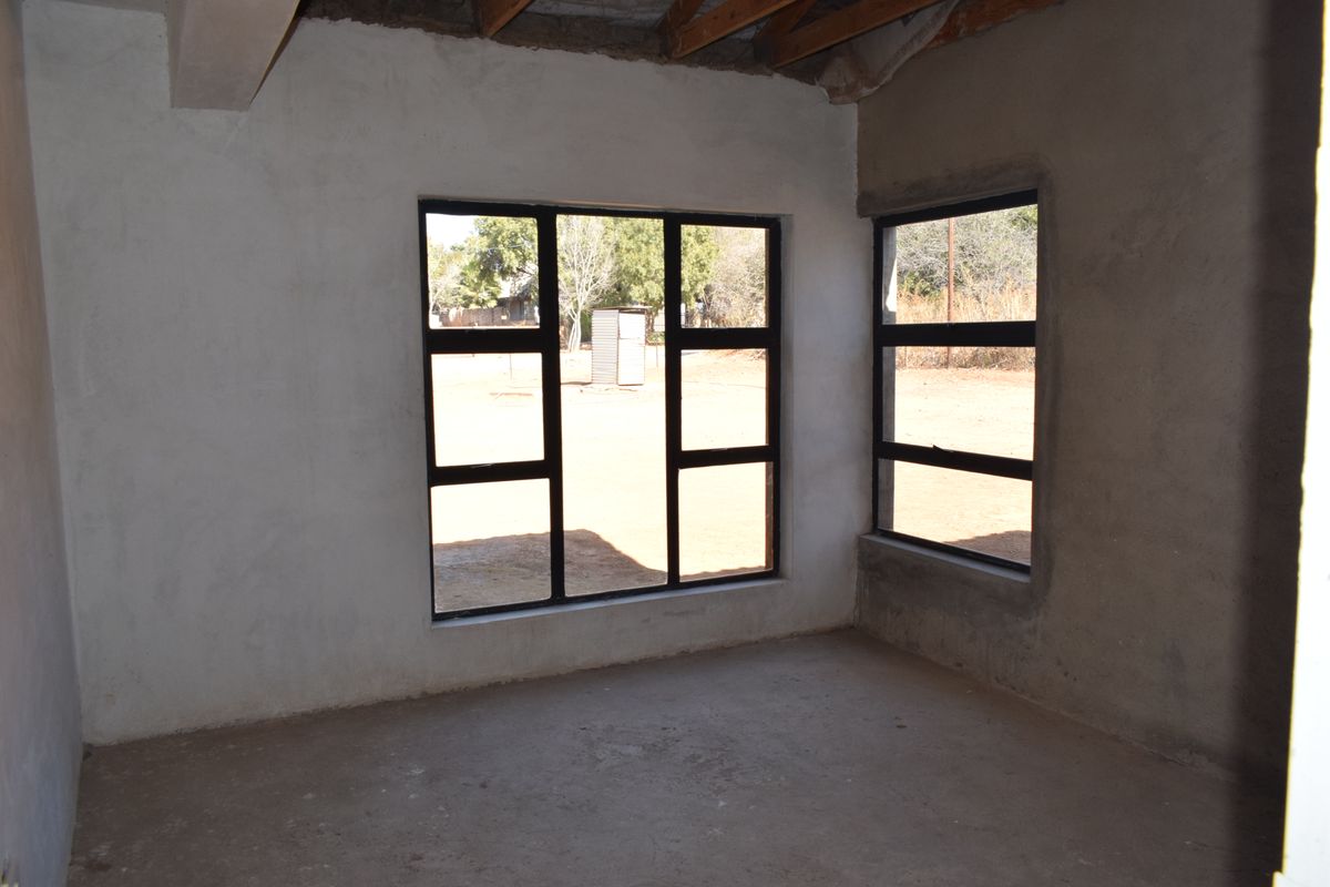 An unfinished bedroom space featuring exposed timber roof trusses, cement screed flooring, and black aluminium window frames, awaiting final interior finishes.