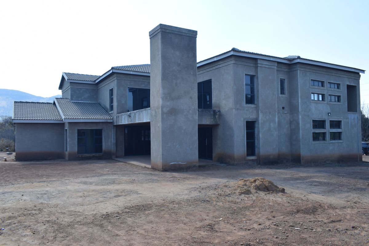 Rear view of a large double-story residential property currently under construction with unfinished exterior plastering and bare surrounding grounds.