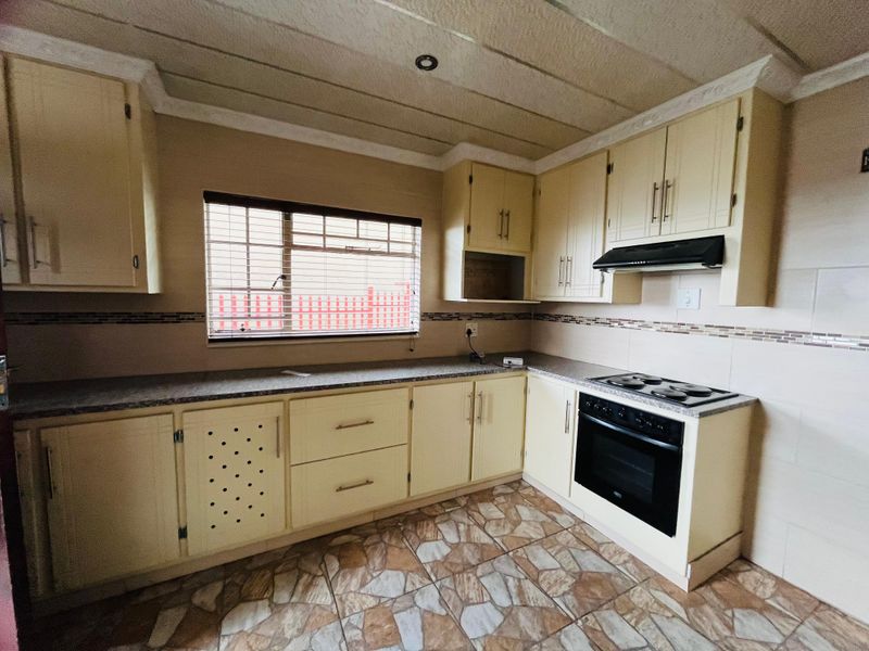 A functional kitchen featuring cream-colored cabinetry, a built-in oven with hob, extractor fan, and tiled flooring with a mosaic backsplash.