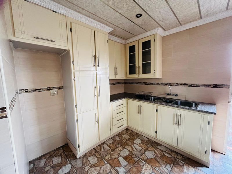 A functional kitchen featuring cream-colored cabinetry, granite-look countertops, a double-basin sink, and tiled flooring with a decorative mosaic backsplash.