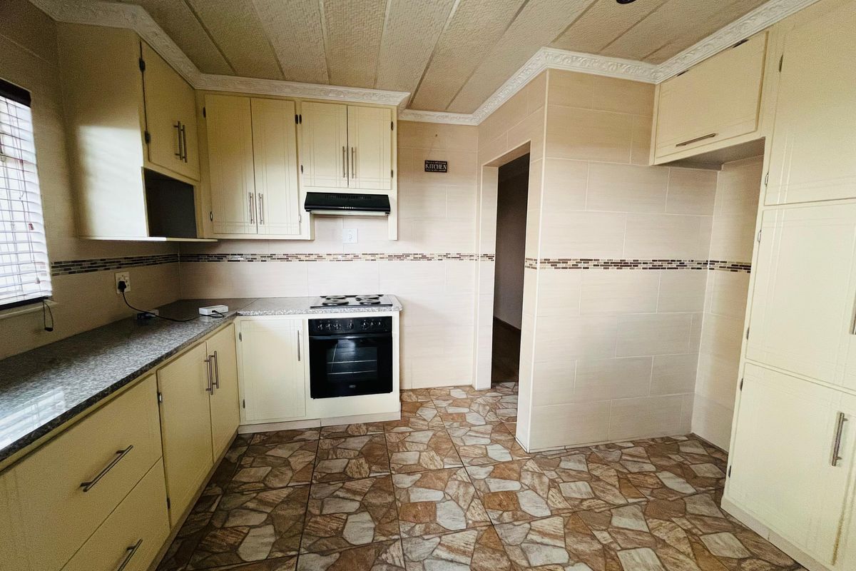A functional kitchen featuring cream cabinetry, granite-look countertops, a built-in oven and hob, and tiled flooring throughout.