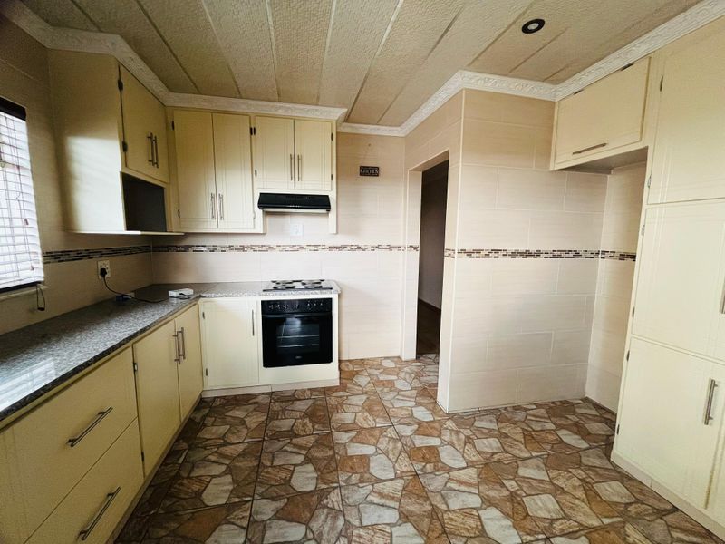 A functional kitchen featuring cream cabinetry, granite-look countertops, a built-in oven and hob, and tiled flooring throughout.