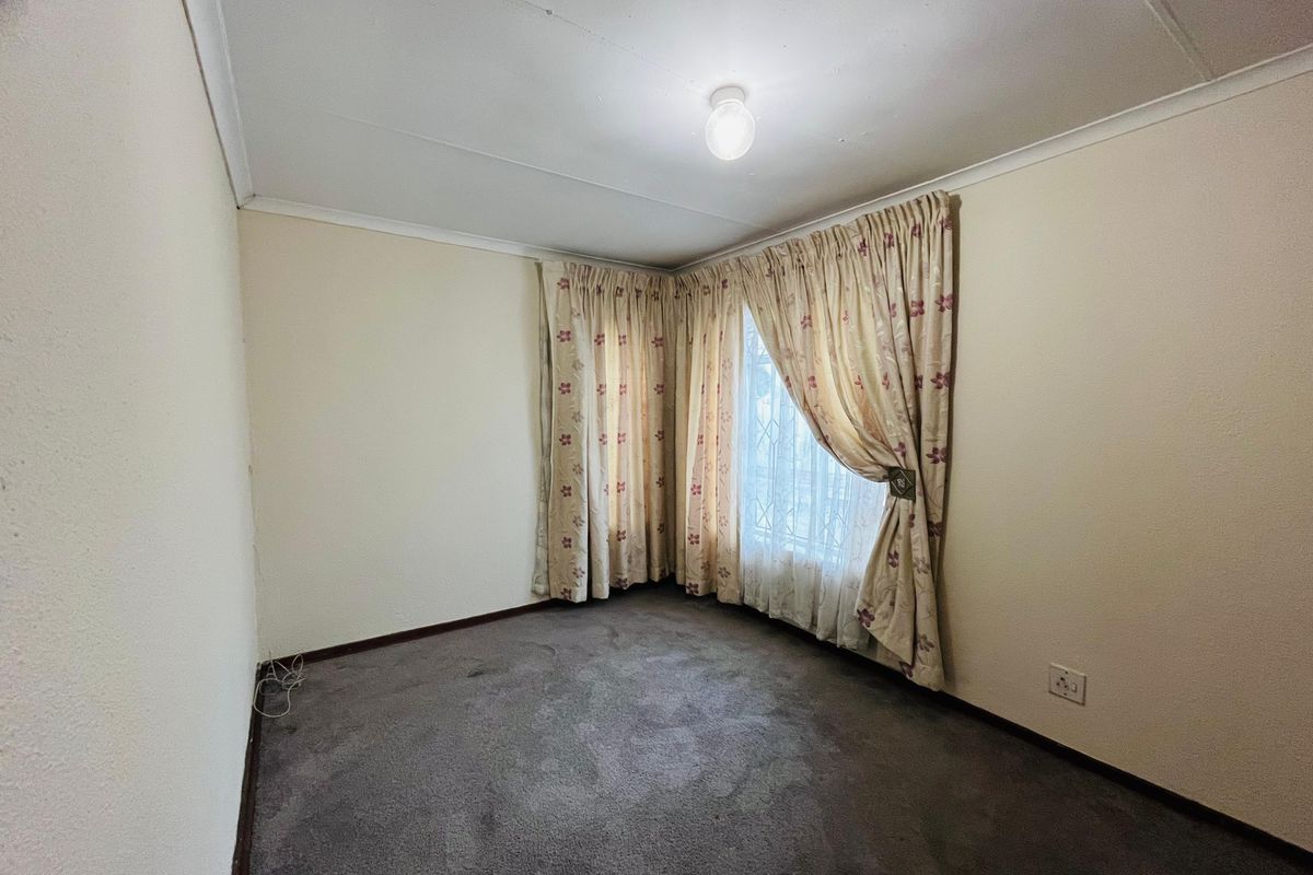 A vacant bedroom featuring grey carpeting, neutral walls, and a window with fitted curtain tracks.