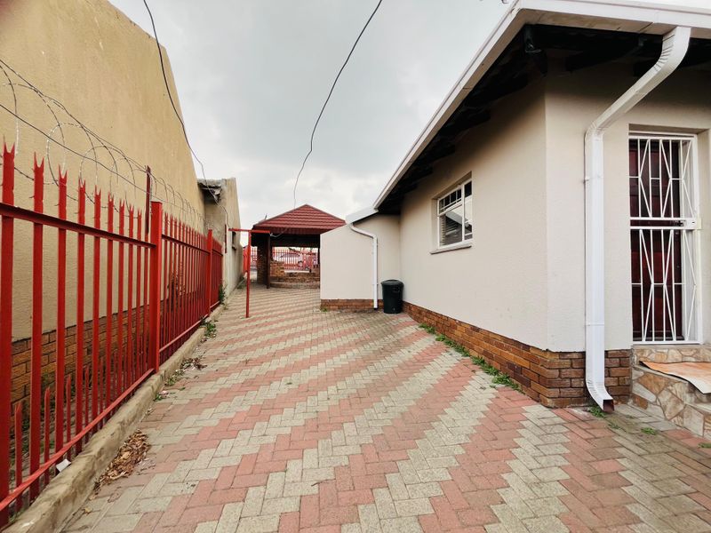 Side exterior view showing paved driveway, red metal security fencing with razor wire, and a covered outdoor structure in the rear.