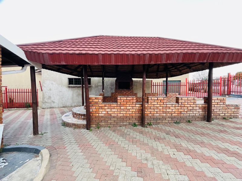 A covered outdoor entertainment area featuring a built-in brick braai, tiled steps, and a thatched roof structure set on a paved patio.