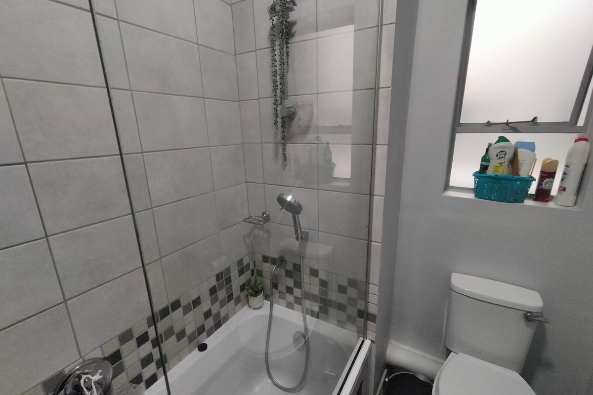 A functional bathroom featuring a shower over the bathtub with a glass screen, tiled splashback, and a standard toilet.