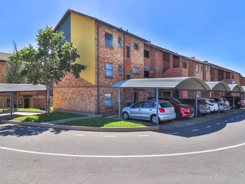 Exterior view of a multi-story face brick apartment complex featuring covered parking bays and paved driveway access.