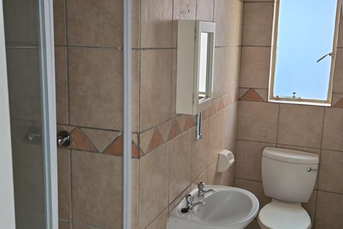 A functional bathroom featuring a shower enclosure, pedestal basin, and toilet with neutral floor-to-ceiling tiling.