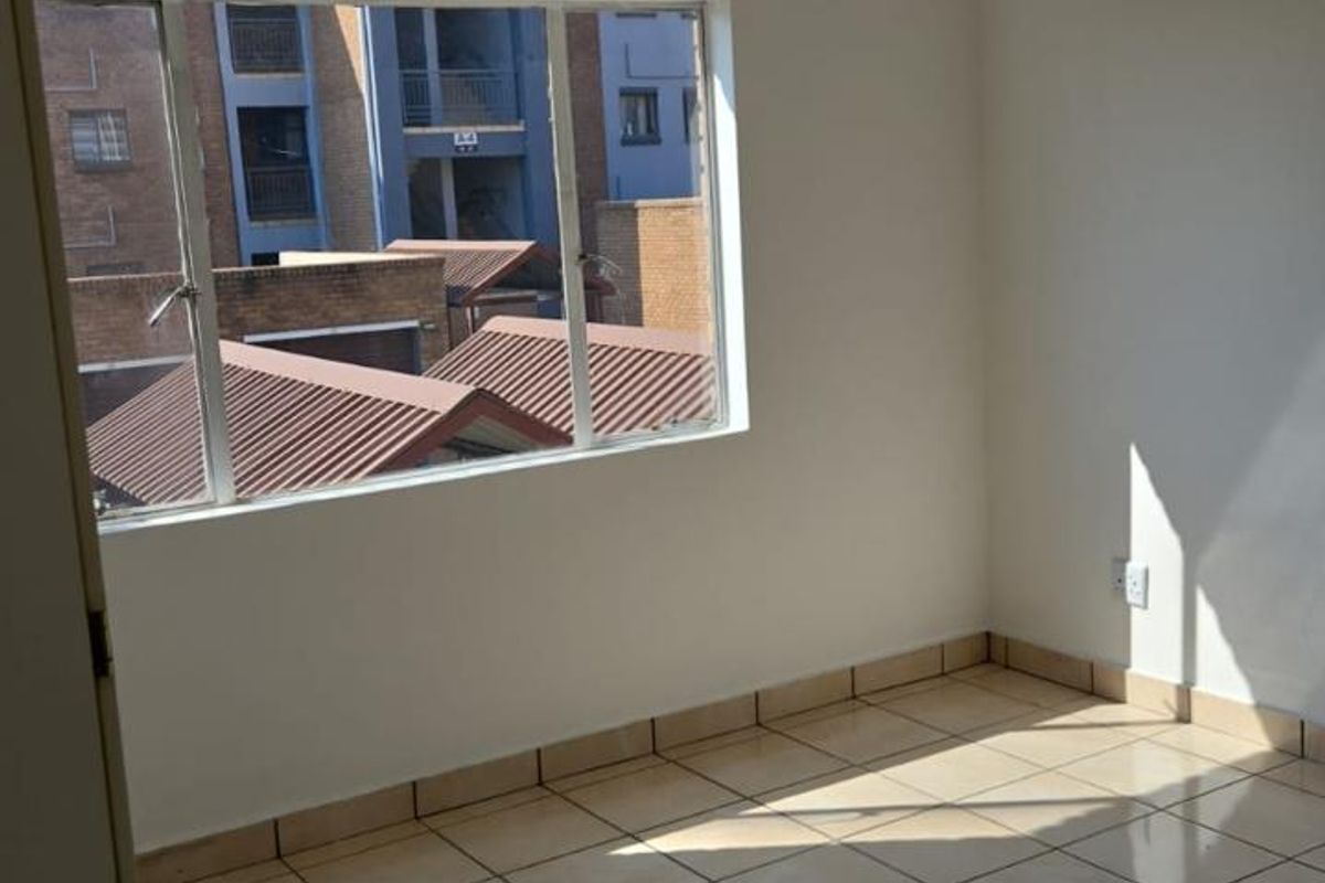 A bright, empty bedroom featuring neutral ceramic floor tiles, a large window with exterior views, and a simple ceiling-mounted light fixture.