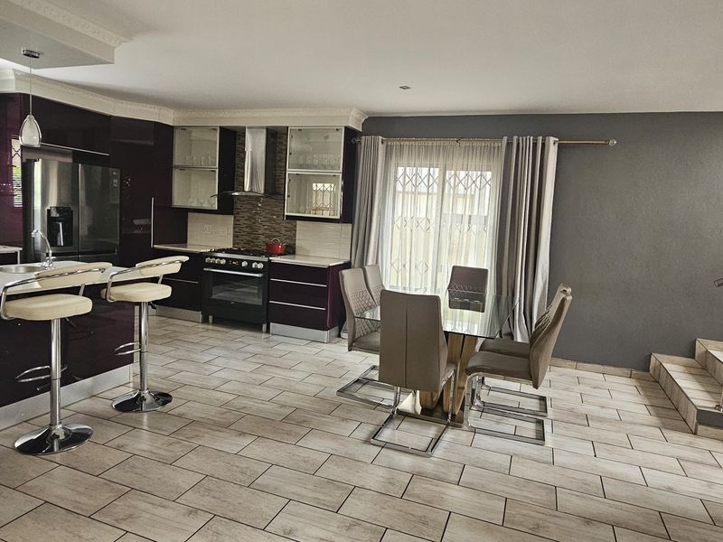Spacious open-plan kitchen and dining area featuring modern dark cabinetry, a central island, tiled flooring, and an adjacent staircase with a contemporary metal railing.