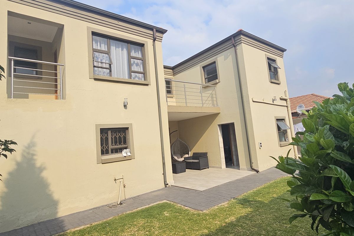 Rear view of a double-story house featuring a covered patio, upper-level balcony with stainless steel railings, and a paved garden area.