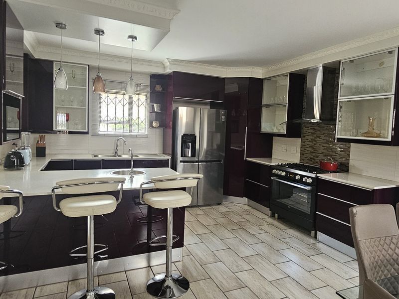 Modern kitchen featuring dark high-gloss cabinetry, stone countertops, a central island with breakfast bar, and integrated appliances with tiled flooring.