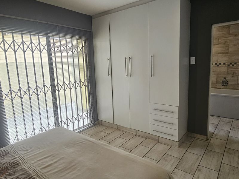 A well-maintained bedroom featuring built-in cupboards, tiled flooring, and a sliding door with a security gate, leading to an en-suite bathroom.