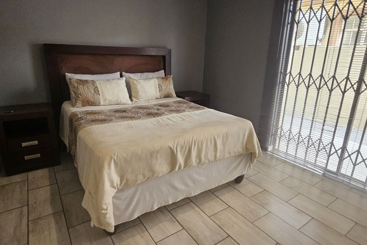 A well-maintained bedroom featuring tiled flooring, neutral wall tones, and a sliding glass door with security gate providing access to the exterior.