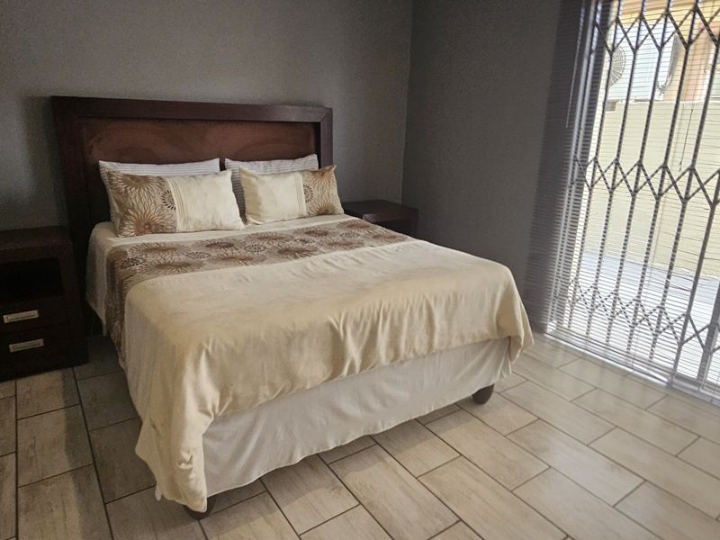 A well-maintained bedroom featuring tiled flooring, neutral wall tones, and a sliding glass door with security gate providing access to the exterior.