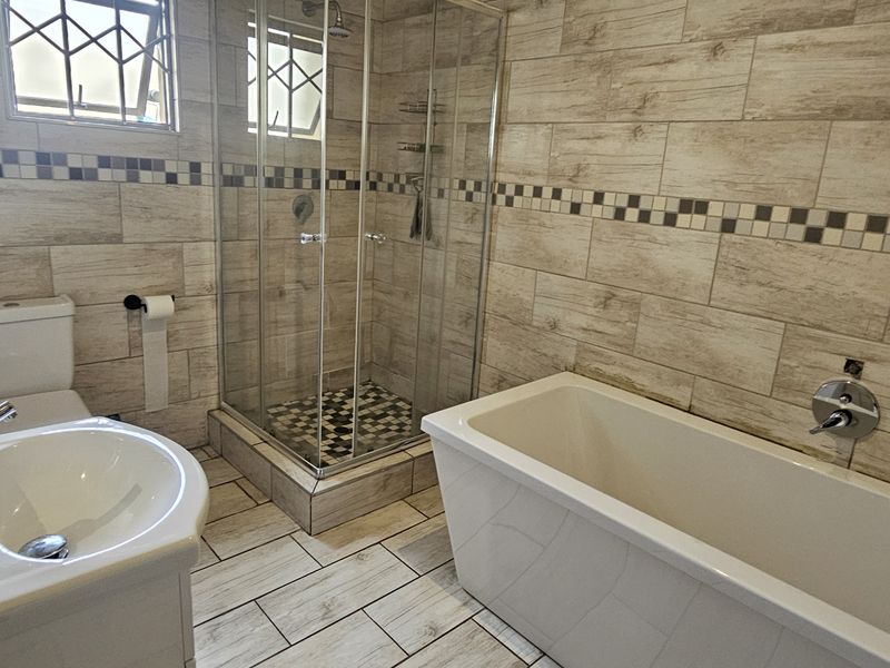 Modern bathroom featuring a glass shower enclosure, a freestanding bathtub, a pedestal basin, and neutral wood-look wall and floor tiling.
