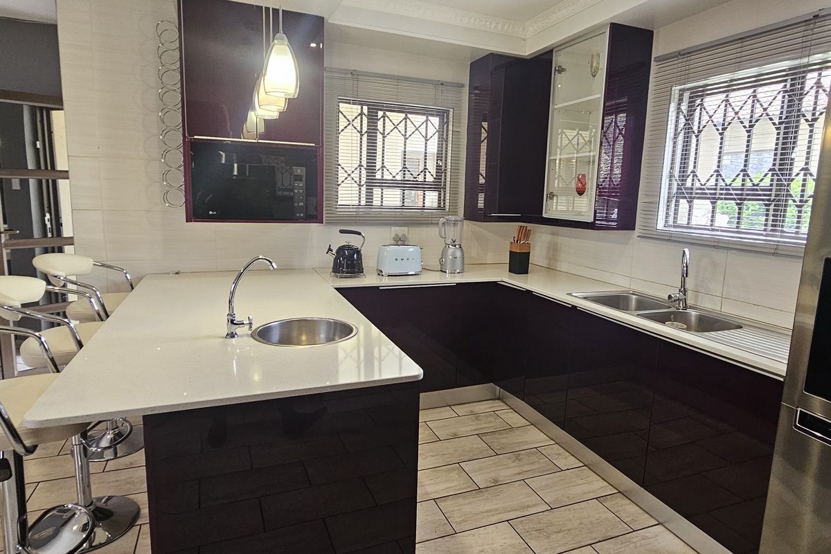 Modern kitchen featuring high-gloss cabinetry, quartz countertops, a breakfast bar, and integrated appliances with tiled flooring and security-fitted windows.