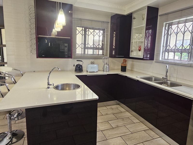 Modern kitchen featuring high-gloss cabinetry, quartz countertops, a breakfast bar, and integrated appliances with tiled flooring and security-fitted windows.